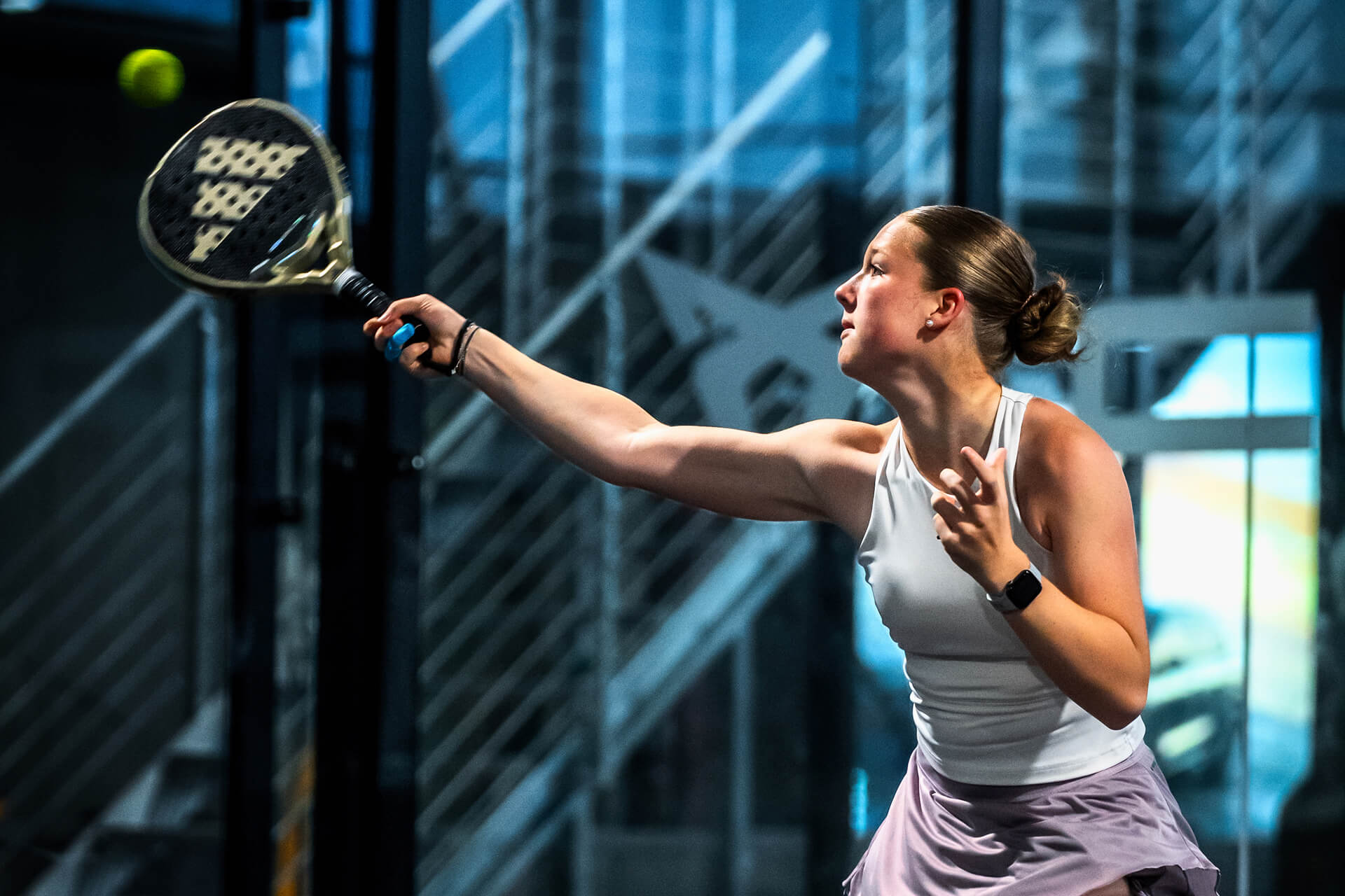 Junge Frau in der Padel-Halle. Sie schlägt gerade den Ball in der Luft