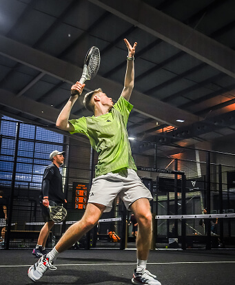 Padel Spieler mit grünem Trikot hält den Schläger hoch und erwartet einen Ball