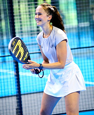 Junge Frau mit hellem T-Shirt und weißem kurzen Rock erwartet freudig den Ball beim Padel spielen