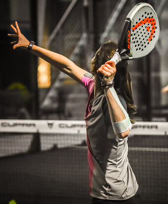 Frau in pink-grauem Trikot hält den Schläger hoch und erwartet einen Ball